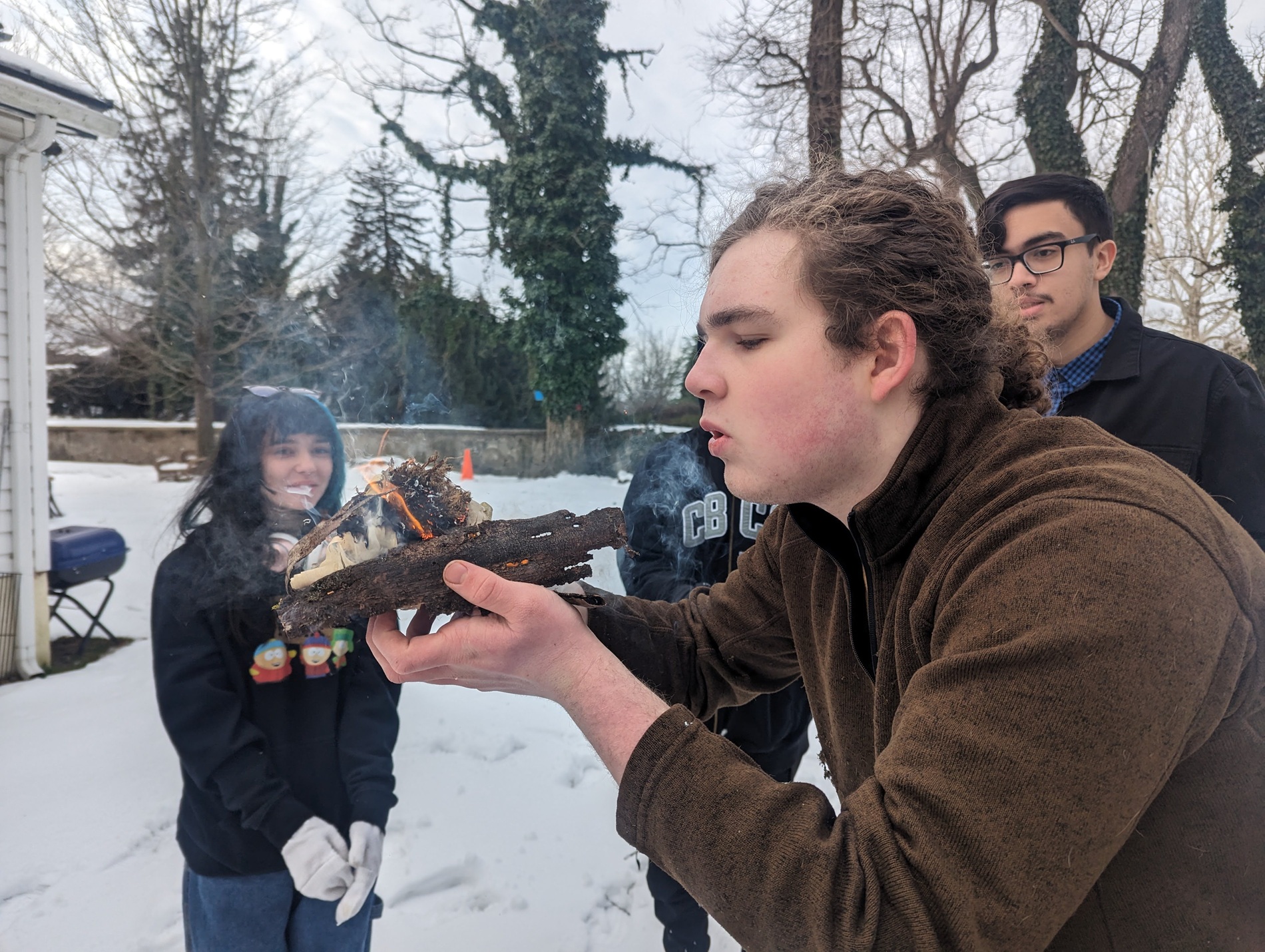 Teens outside in the winter, working on starting a fire